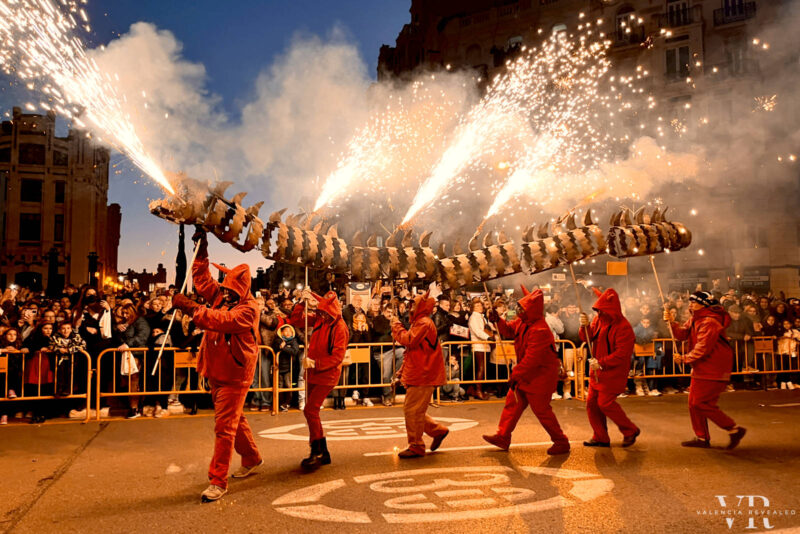 Several people in red costumes parade a fire dragon