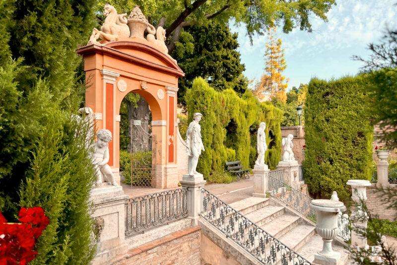 An orange gate with marble statues and tree at Monforte Gardens in Valencia