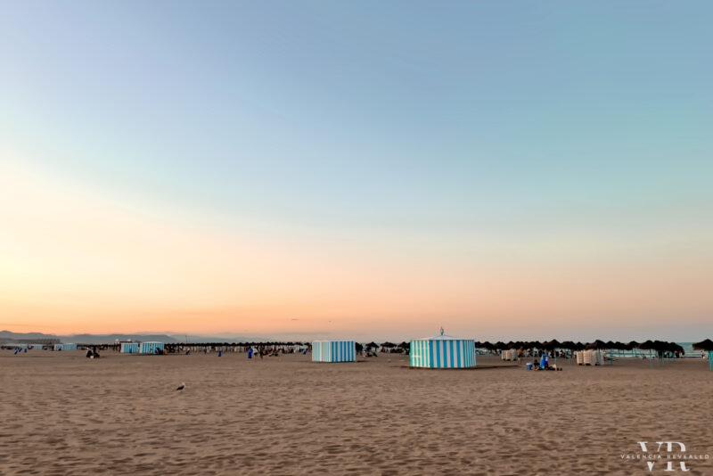 A wide sand beach with blue and white tents near El Cabanyal, one of the best neighborhoods to stay in Valencia