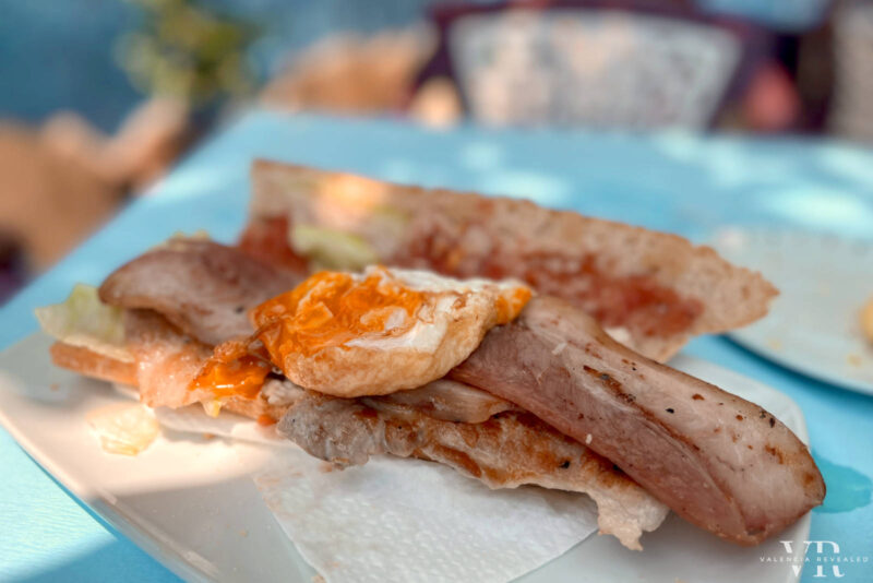 An open bocadillo on a white plate on a blue tablecloth