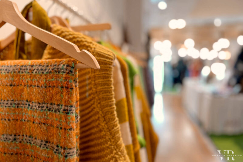 A hanger with orange and green sweaters and scarves