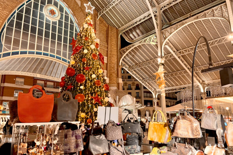 Bags on display at a Christmas market stall inside the covered Colón Market with a Christmas tree in the background