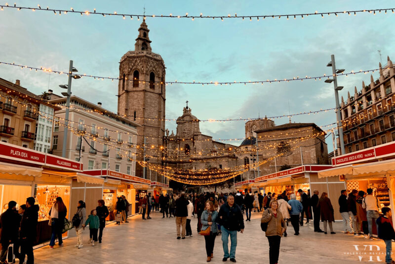 People walking among the stalls of a Chistmas market with the Valencia cathedral in the background
