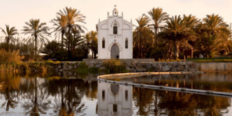 A beautiful white hermitage, framed by graceful palm trees, reflected in a lake
