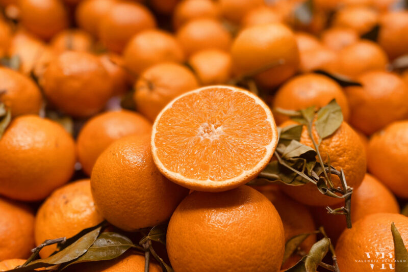 A pile of Valencian oranges, one of which is sliced in half
